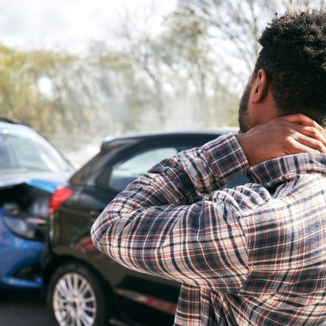 a man with his neck and back in front of a wrecked car